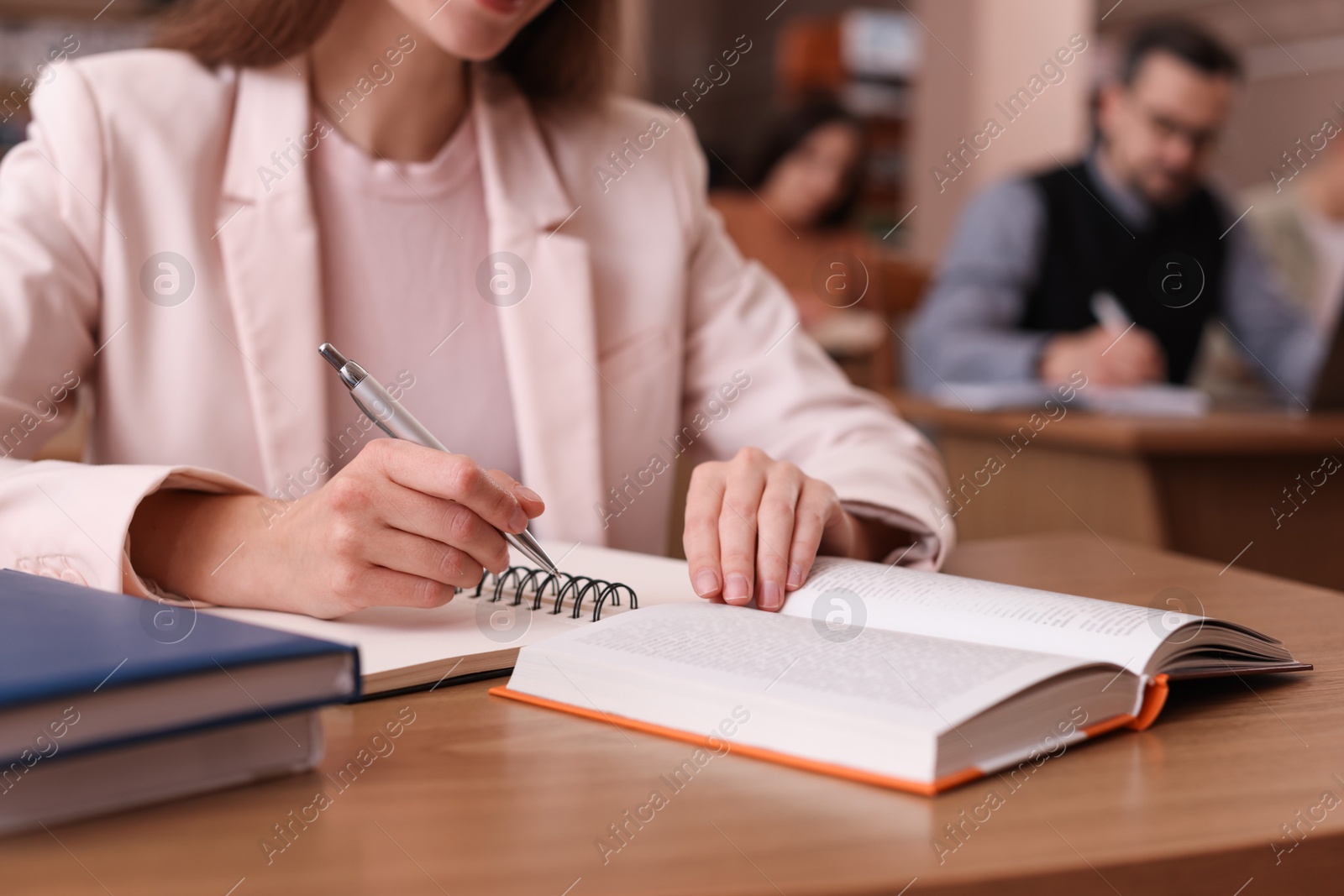 Photo of Woman reading book and taking notes at desk in library, closeup