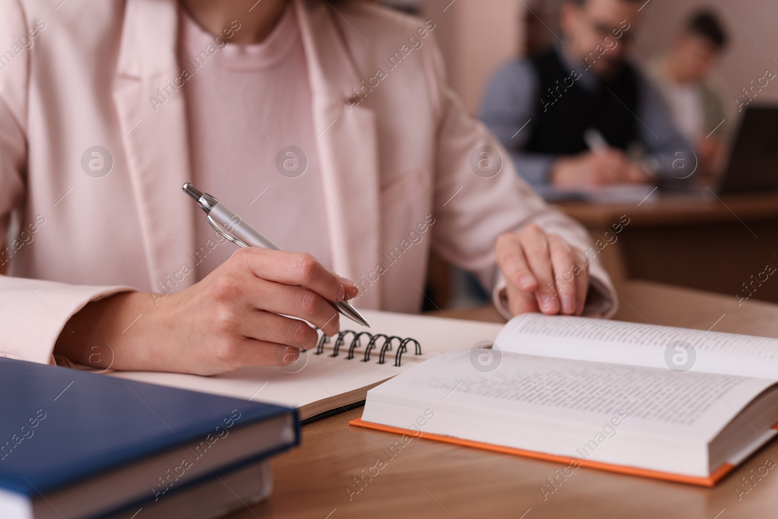 Photo of Woman reading book and taking notes at desk in library, closeup