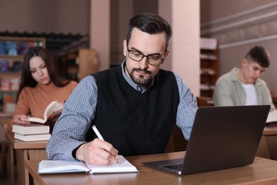 Photo of Man with laptop taking notes at desk in public library