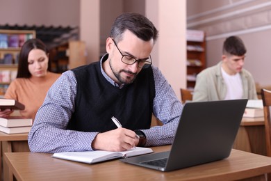 Photo of Man with laptop taking notes at desk in public library