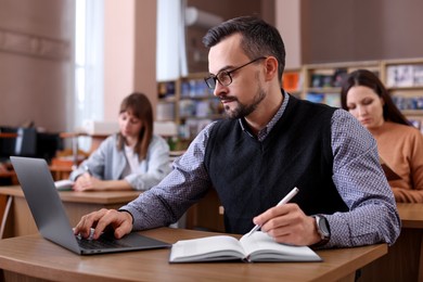 Photo of Man with laptop taking notes at desk in public library