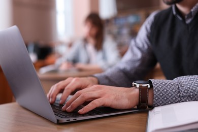 Photo of Man typing on laptop at desk in library, closeup