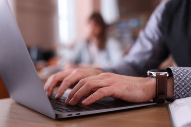 Photo of Man typing on laptop at desk in library, closeup