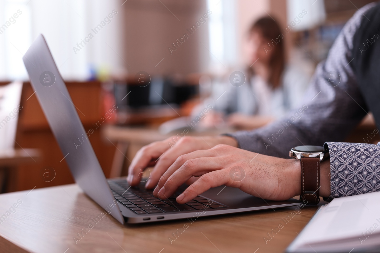 Photo of Man typing on laptop at desk in library, closeup