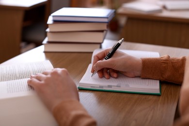 Photo of Woman reading book and taking notes at desk in library, closeup