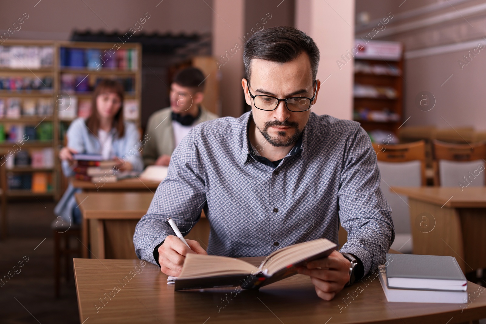 Photo of Handsome man reading book and taking notes at desk in public library