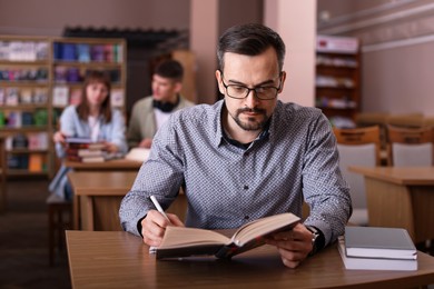 Photo of Handsome man reading book and taking notes at desk in public library