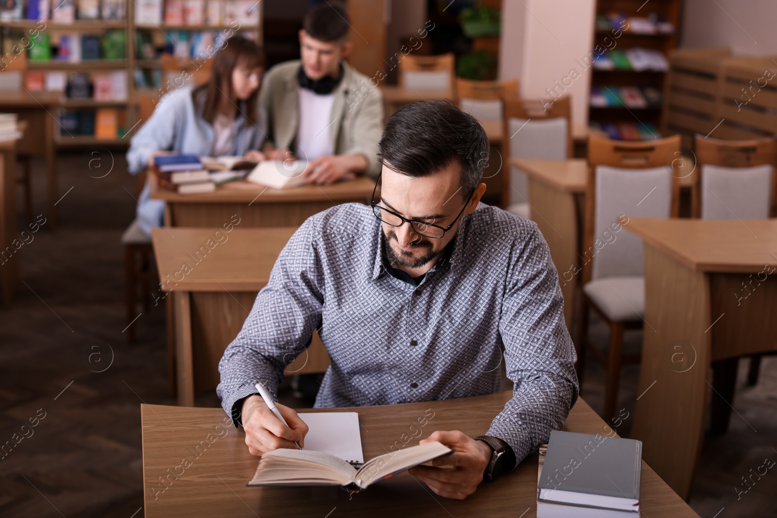 Photo of Handsome man reading book and taking notes at desk in public library