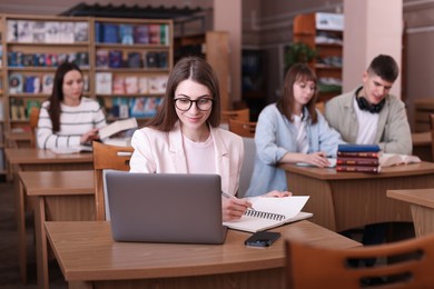 Photo of Beautiful woman with laptop taking notes at desk in public library