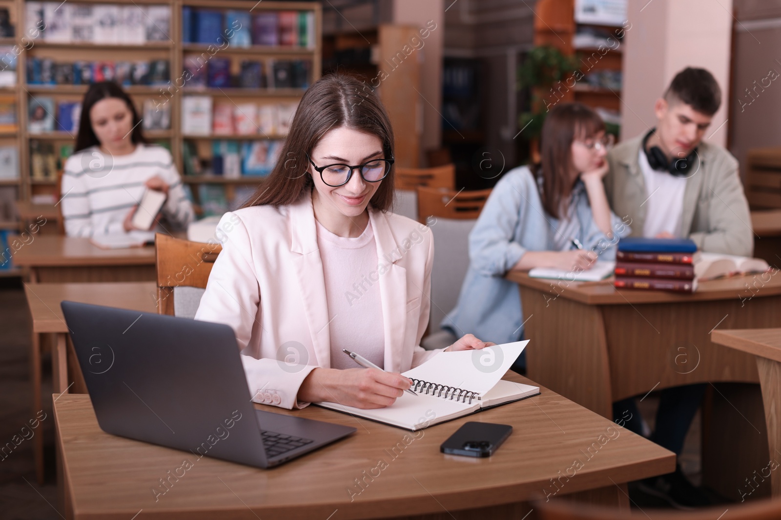 Photo of Beautiful woman with laptop taking notes at desk in public library