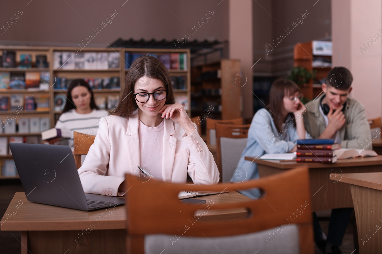 Photo of Beautiful woman with laptop taking notes at desk in public library