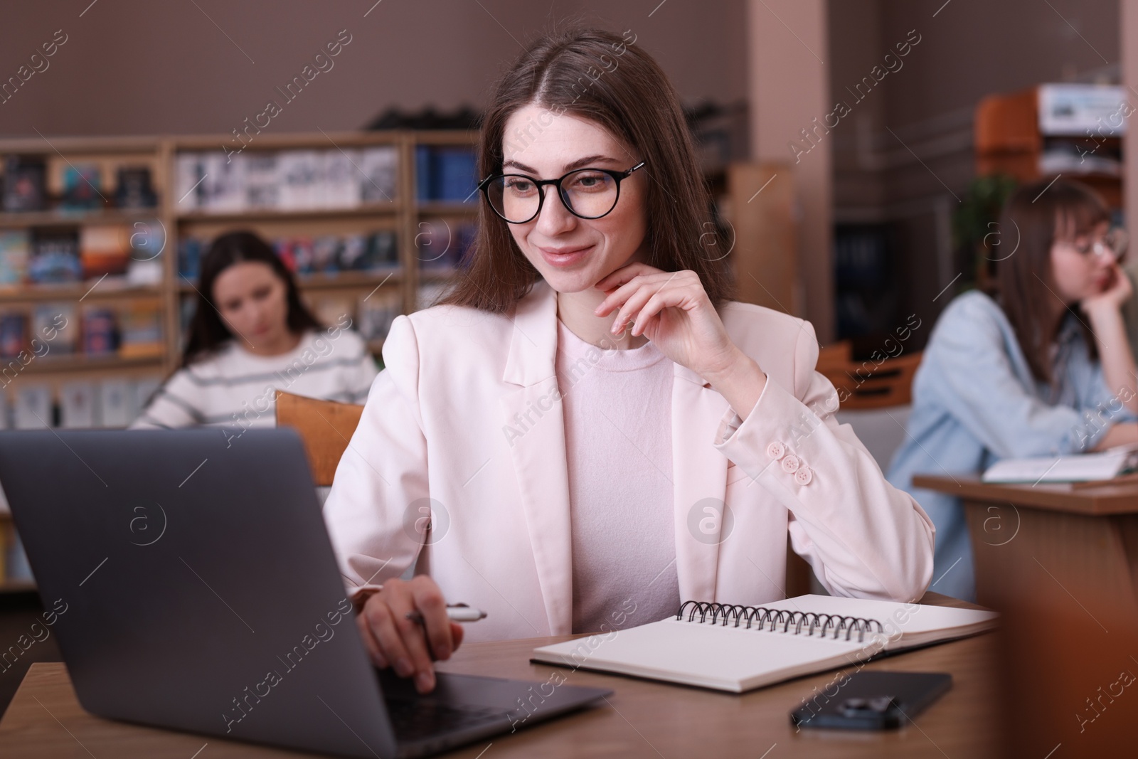 Photo of Beautiful woman with laptop taking notes at desk in public library