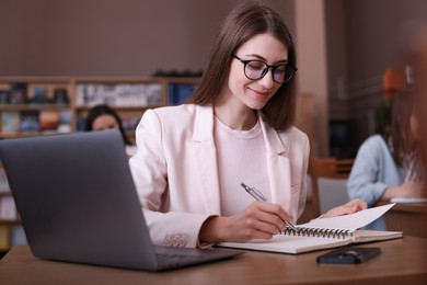 Photo of Beautiful woman with laptop taking notes at desk in public library