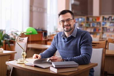 Photo of Portrait of smiling man with books at desk in library