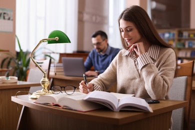 Photo of Beautiful woman reading book and taking notes at desk in public library