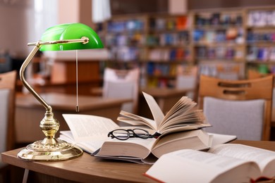 Photo of Different books, glasses and beautiful lamp on wooden desk in library