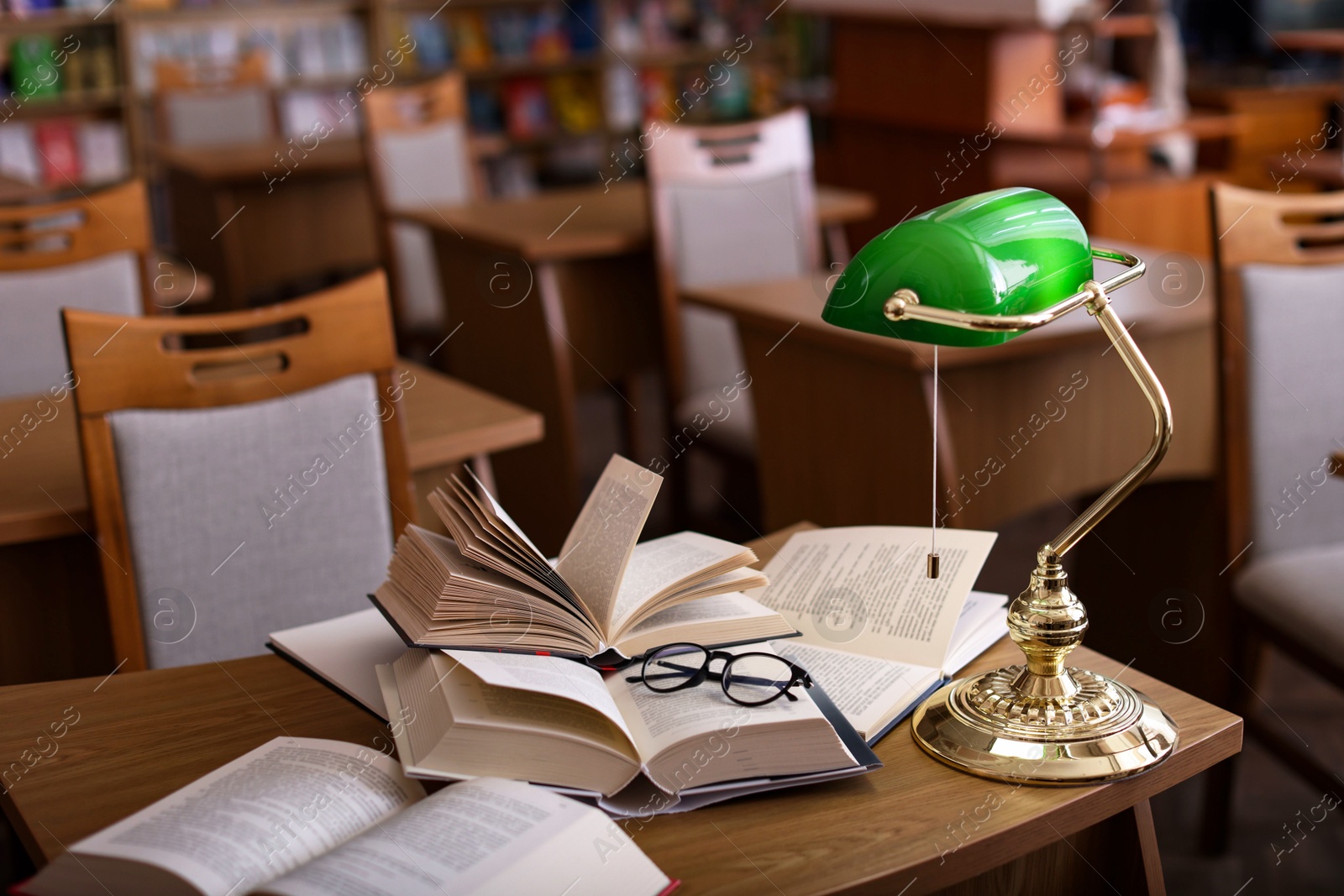 Photo of Different books, glasses and beautiful lamp on wooden desk in library