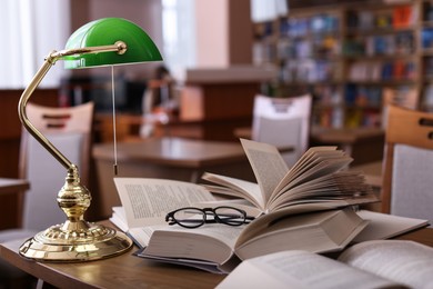 Photo of Different books, glasses and beautiful lamp on wooden desk in library