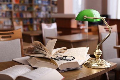 Photo of Different books, glasses and beautiful lamp on wooden desk in library