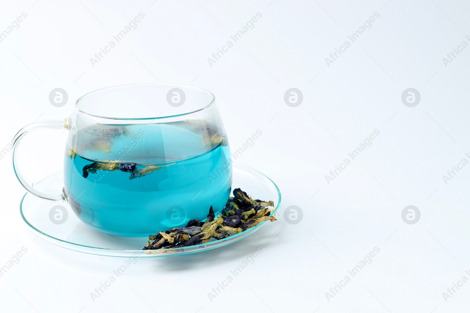 Photo of Fresh butterfly pea flower tea in cup and dry petals on white table, closeup. Space for text