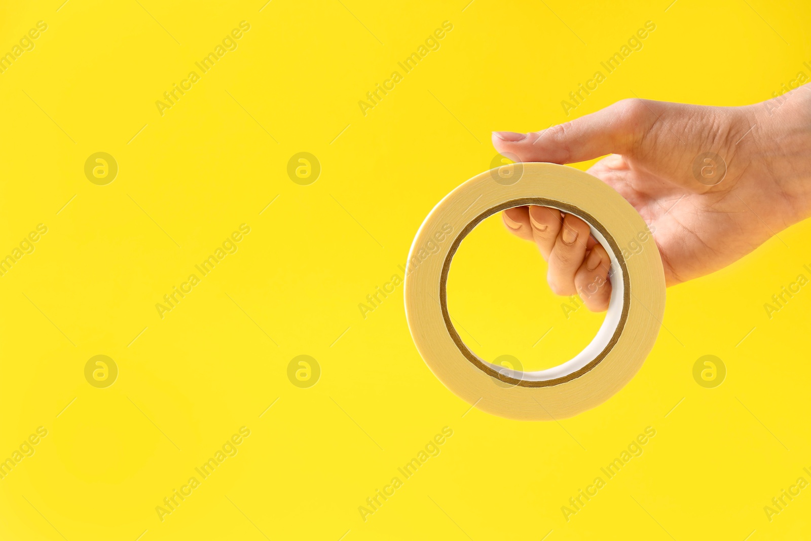 Photo of Woman holding masking tape on yellow background, closeup. Space for text