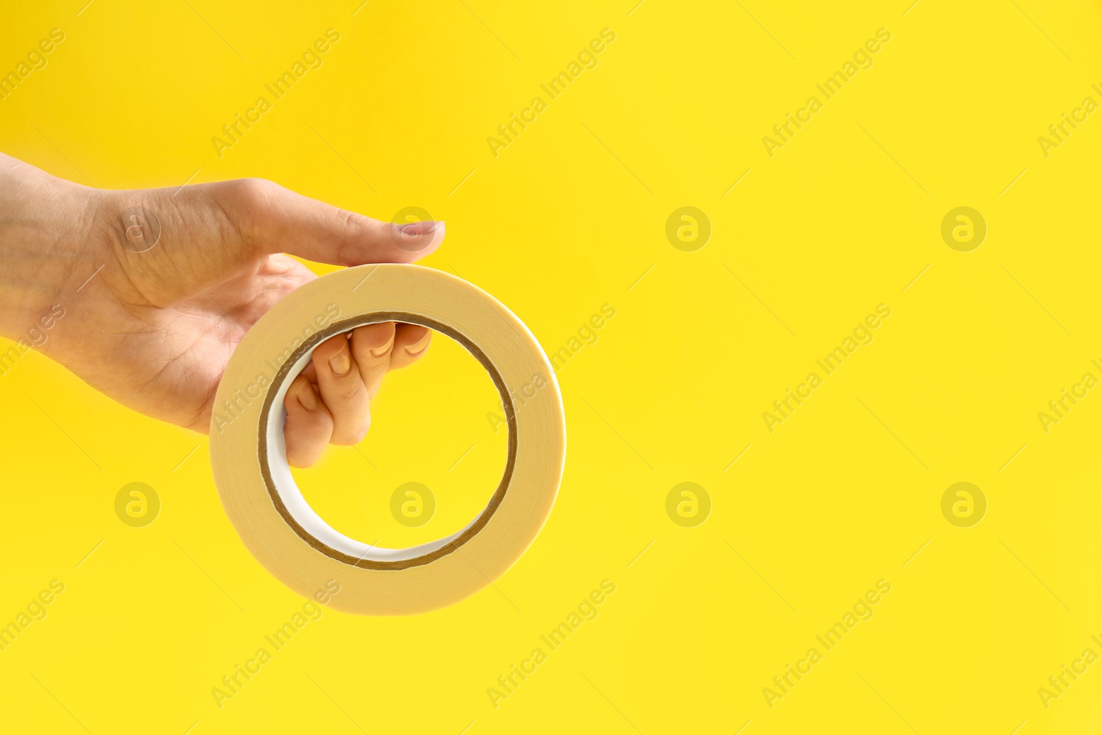 Photo of Woman holding masking tape on yellow background, closeup. Space for text