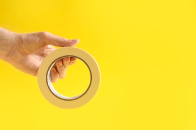 Woman holding masking tape on yellow background, closeup. Space for text