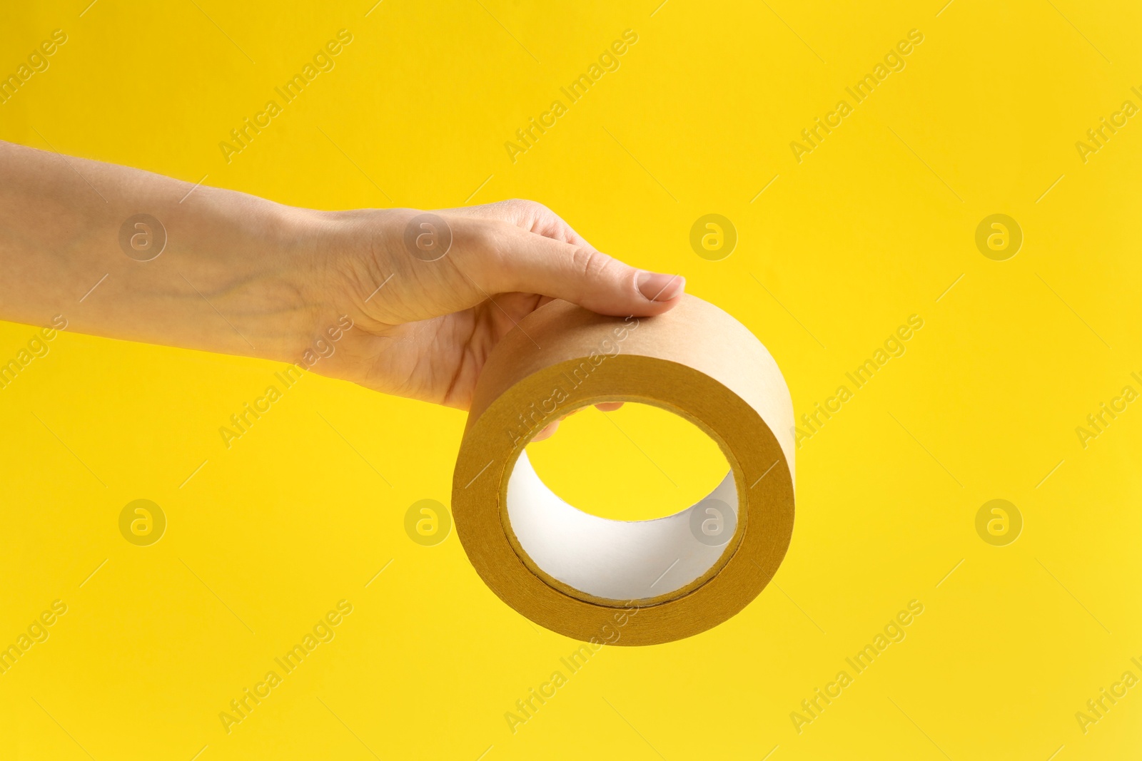 Photo of Woman holding masking tape on yellow background, closeup