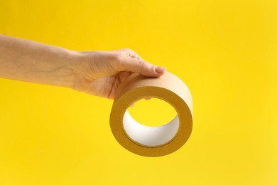 Photo of Woman holding masking tape on yellow background, closeup