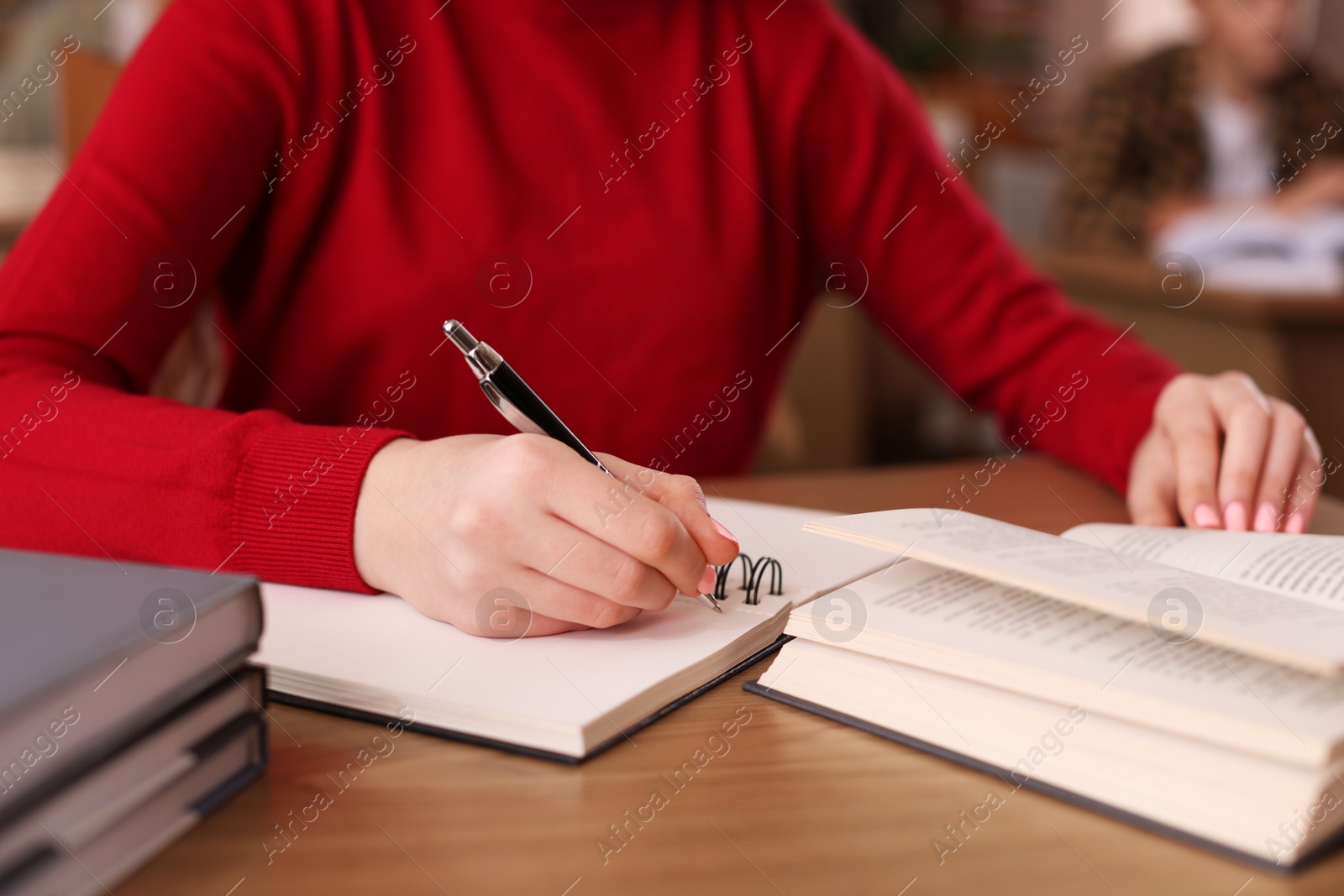 Photo of Girl taking notes at wooden desk in public library, closeup