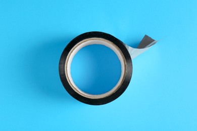 Roll of black adhesive tape on light blue background, top view