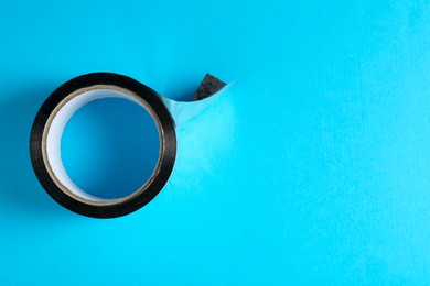 Photo of Roll of black adhesive tape on light blue background, top view. Space for text