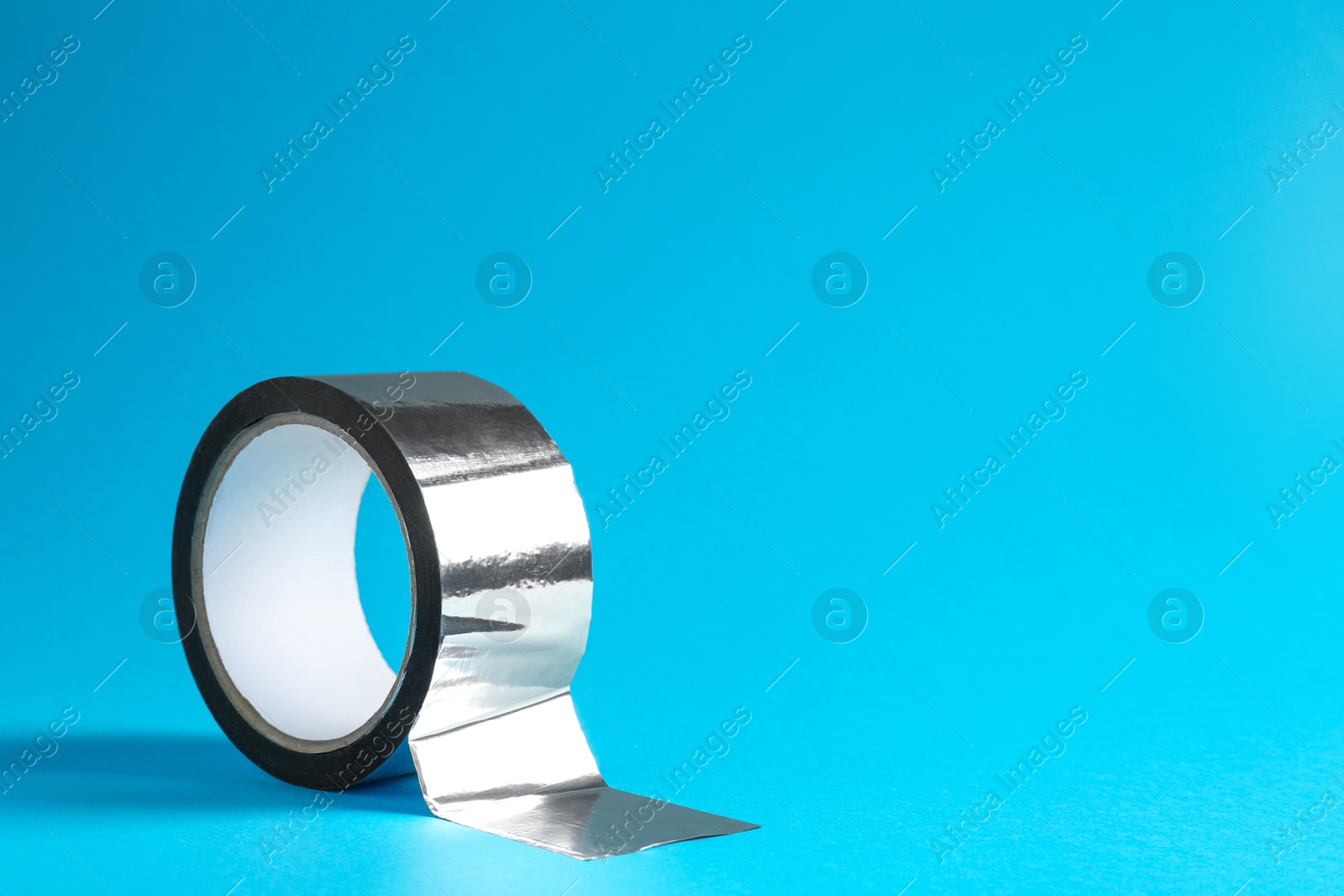 Photo of Roll of silver adhesive tape on light blue background, space for text