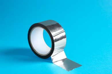 Roll of silver adhesive tape on light blue background