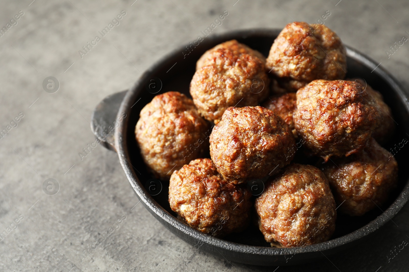 Photo of Tasty meatballs in baking dish on grey table, closeup. Space for text