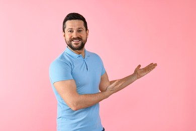 Photo of Happy man welcoming friends or guests on pink background