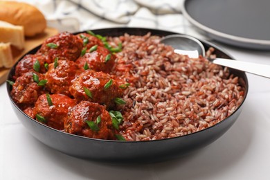 Photo of Tasty meatballs with sauce and brown rice on white tiled table, closeup