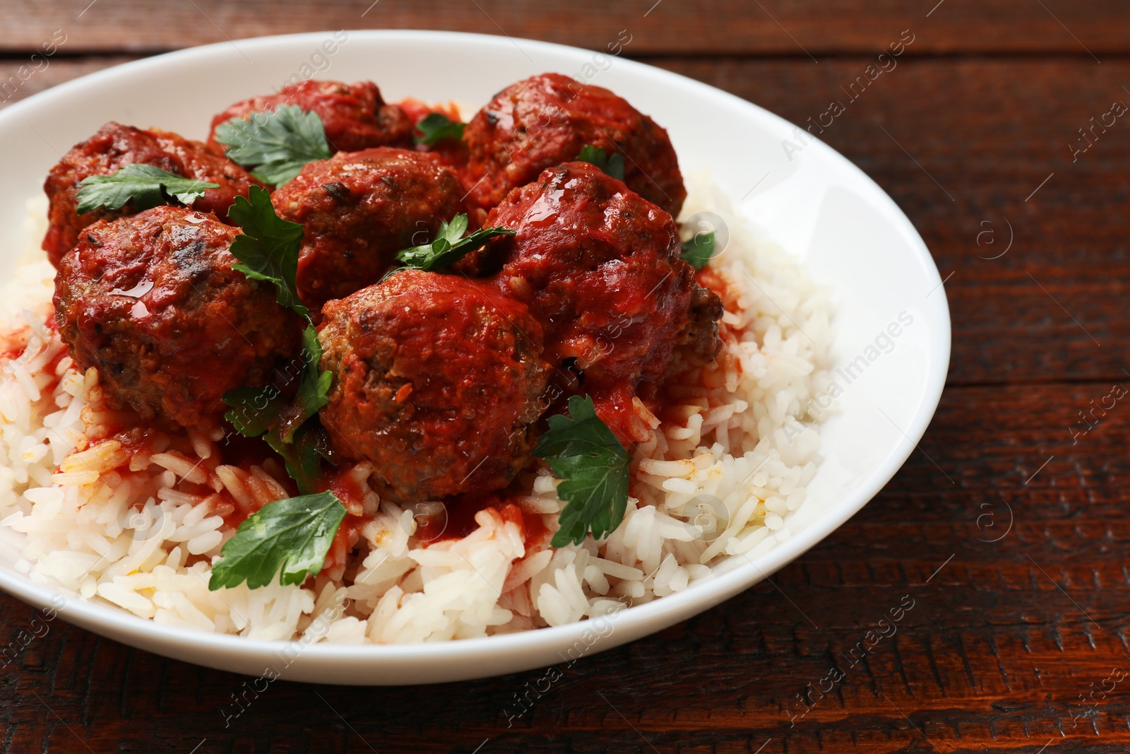 Photo of Tasty meatballs with sauce and rice on wooden table, closeup