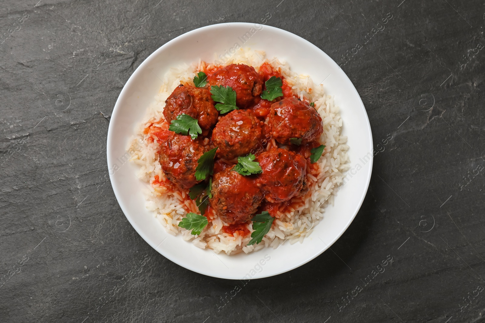 Photo of Tasty meatballs with sauce and rice on black table, top view