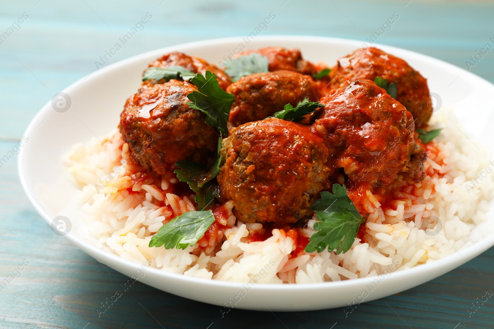 Photo of Tasty meatballs with sauce and rice on light blue wooden table, closeup