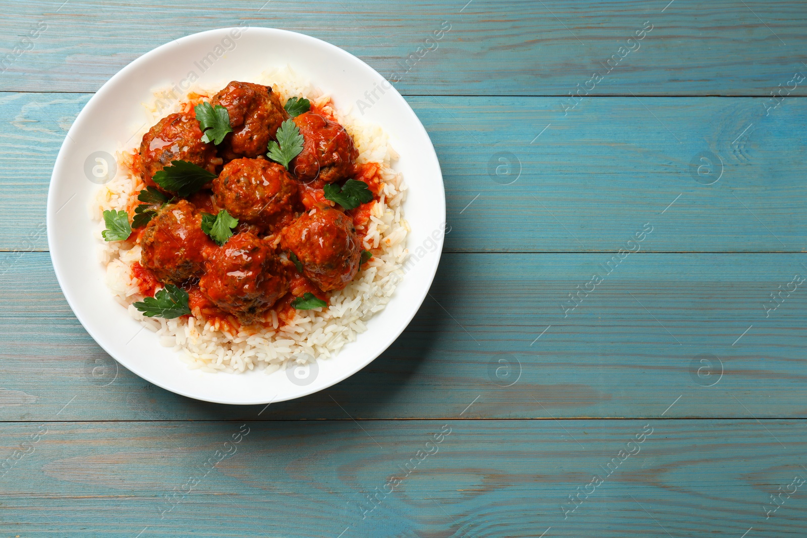 Photo of Tasty meatballs with sauce and rice on light blue wooden table, top view. Space for text