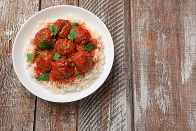 Photo of Tasty meatballs with sauce and rice on wooden table, top view. Space for text