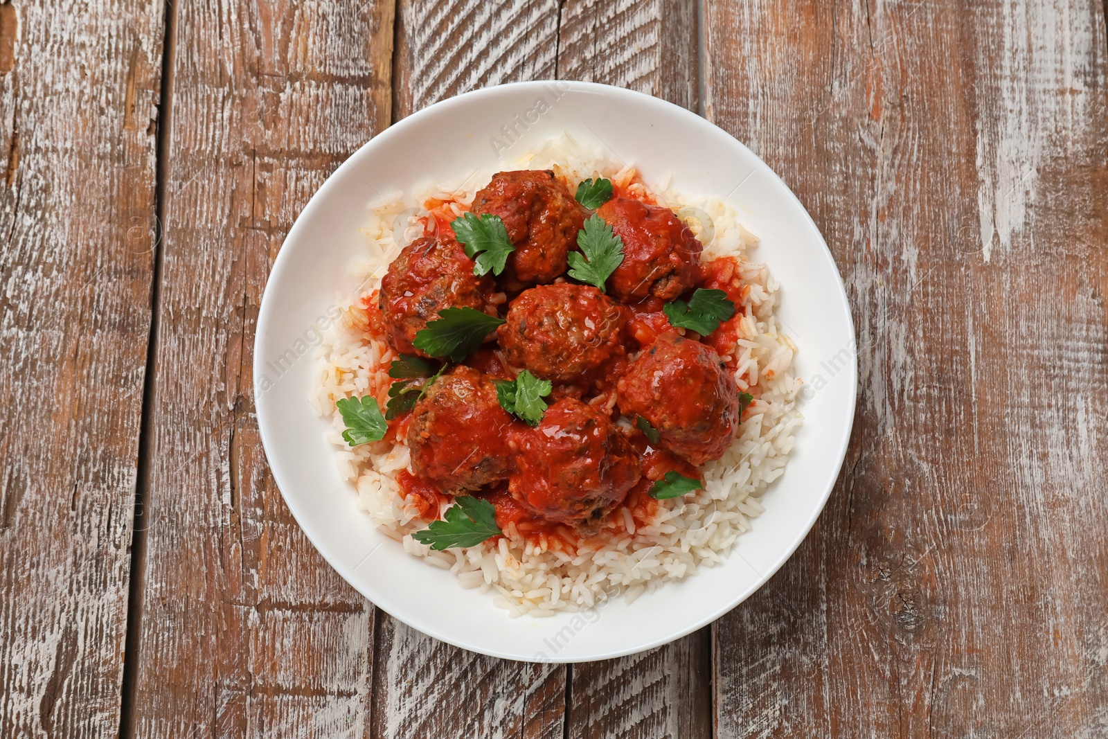 Photo of Tasty meatballs with sauce and rice on wooden table, top view