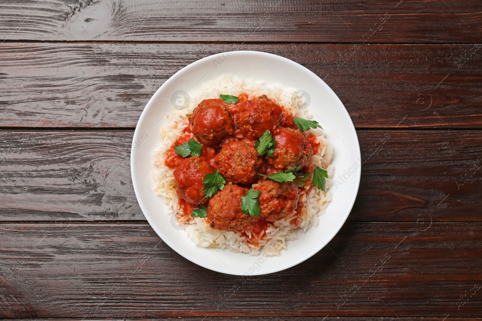 Photo of Tasty meatballs with sauce and rice on wooden table, top view