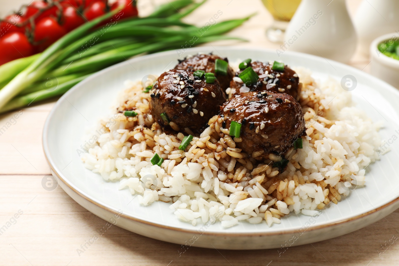 Photo of Delicious rice with meatballs, sauce and green onions on white wooden table, closeup