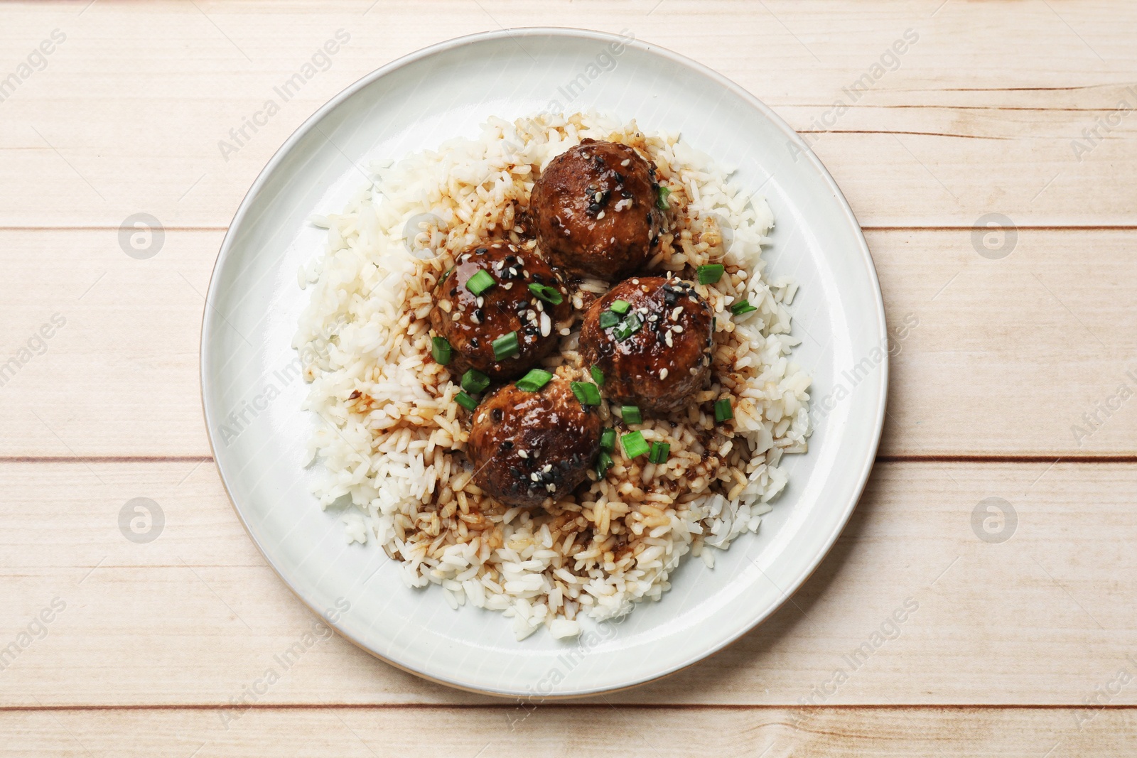 Photo of Delicious rice with meatballs, sauce and green onions on white wooden table, top view