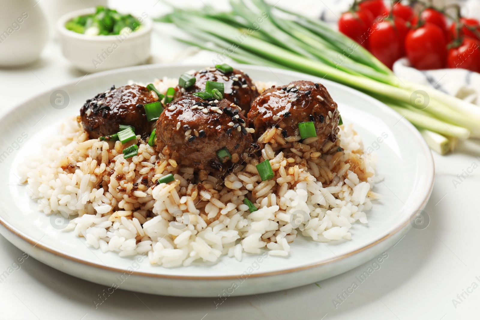 Photo of Delicious rice with meatballs, sauce and green onions on white table, closeup