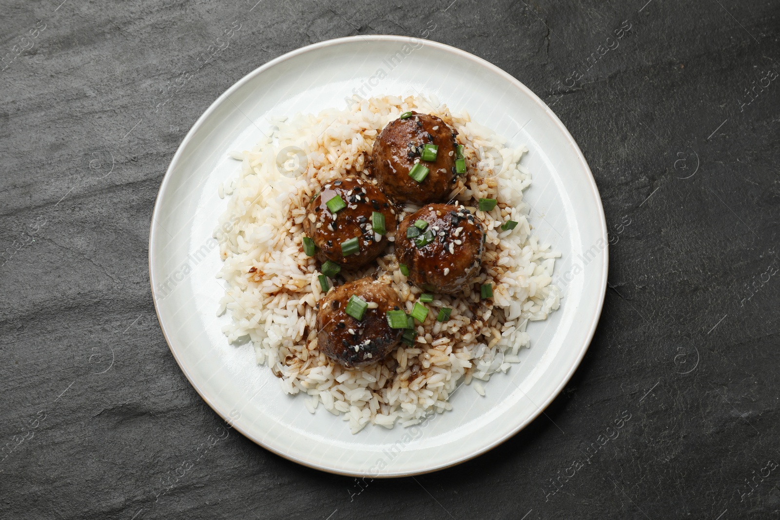 Photo of Delicious rice with meatballs, sauce and green onions on black table, top view