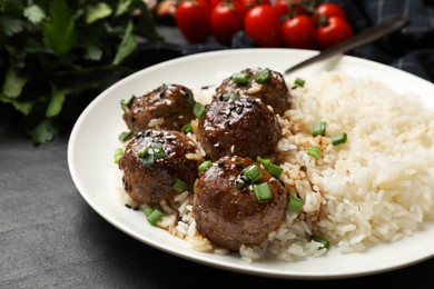 Photo of Delicious rice with meatballs, sauce and green onions on black table, closeup