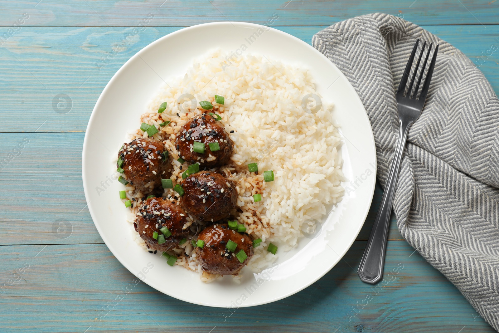 Photo of Delicious rice with meatballs, sauce and green onions on blue wooden table, top view